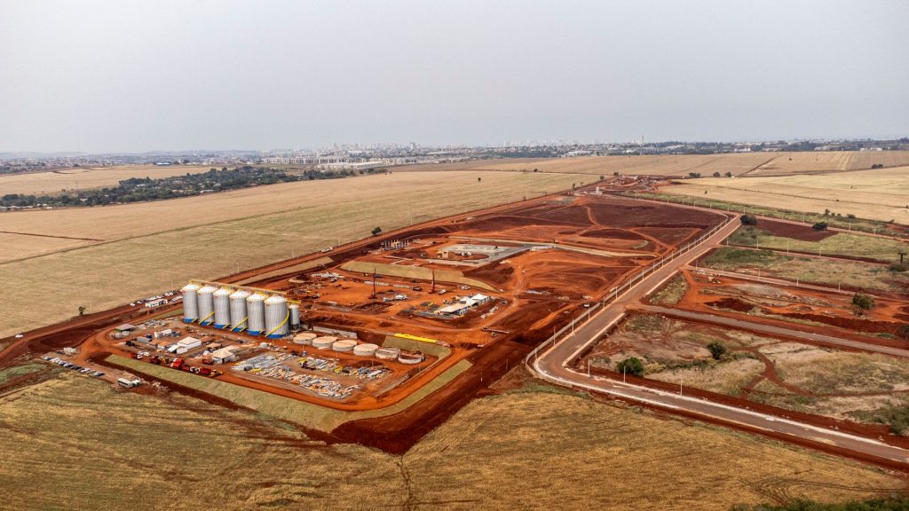 Vista aérea de um amplo canteiro de obras com estruturas e máquinas em uma área de desenvolvimento industrial.