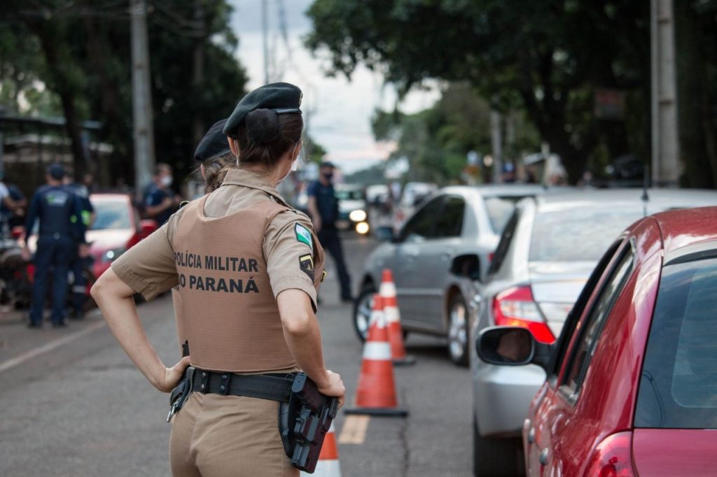 Rondonópolis terá interdições de trânsito perto dos locais de votação Policial visto de costas orienta o trânsito em uma via movimentada.