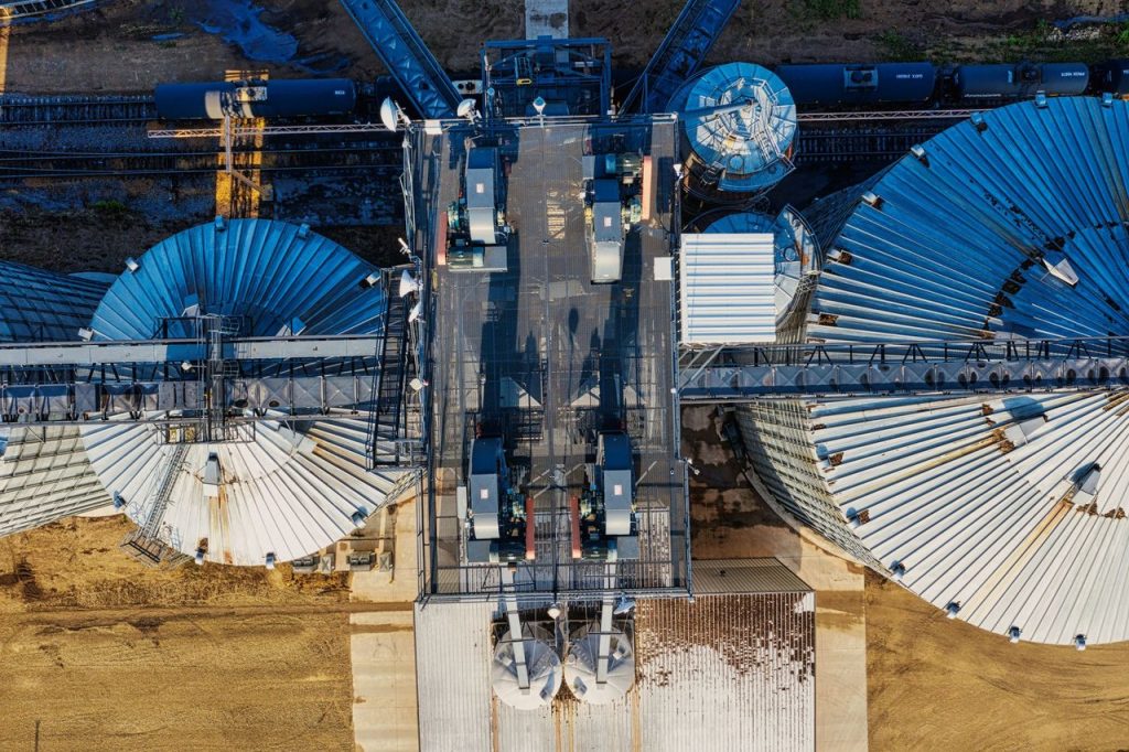 Vista aérea de silos industriais junto a trilhos ferroviários em uma área de armazenagem de grãos.