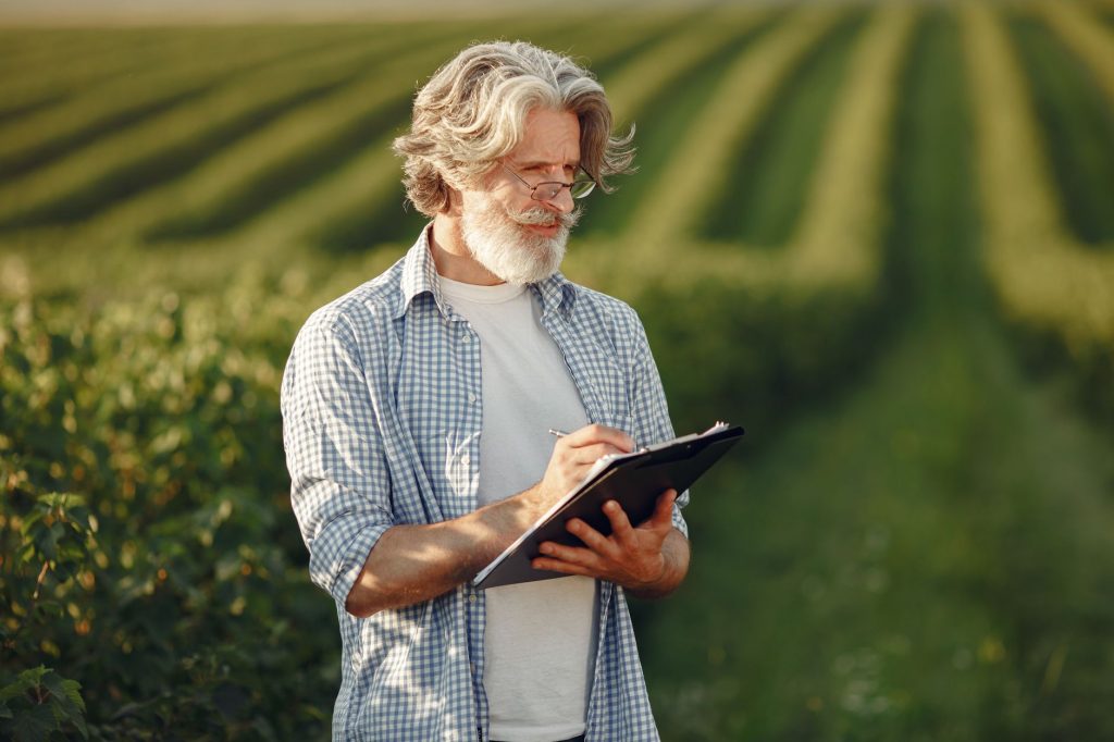 Produtor rural em uma plantação verde, fazendo anotações em uma prancheta.