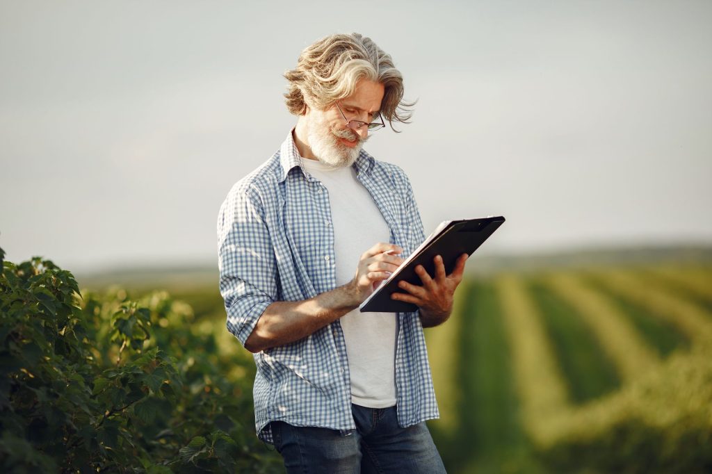 Produtor rural escreve em um caderno em meio a um campo agrícola.
